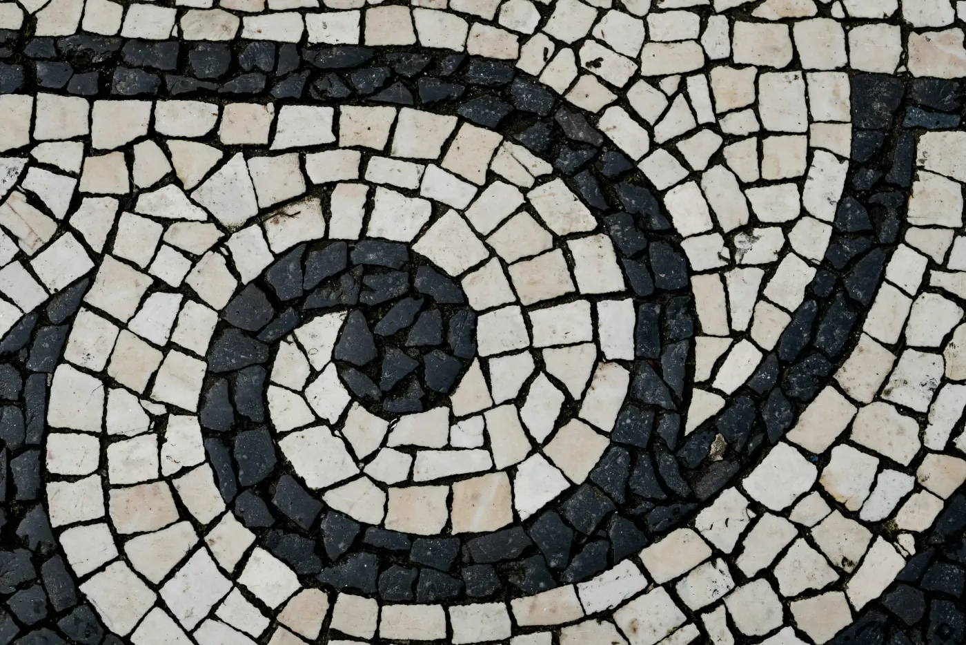 Traditional Portuguese calçada paving — hand-cut white limestone and dark basalt set in a spiral.