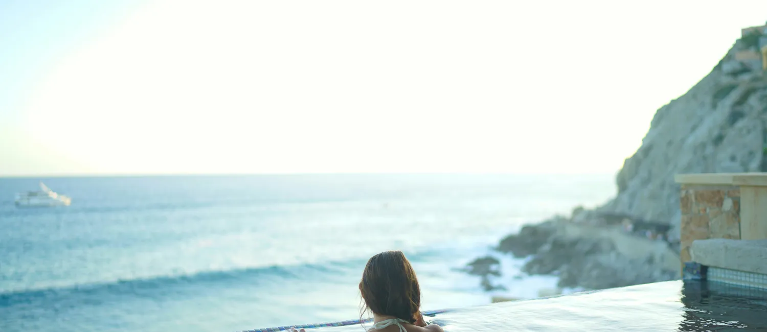 A swimmer at the edge of an infinity pool looking out over the sea in late afternoon light.