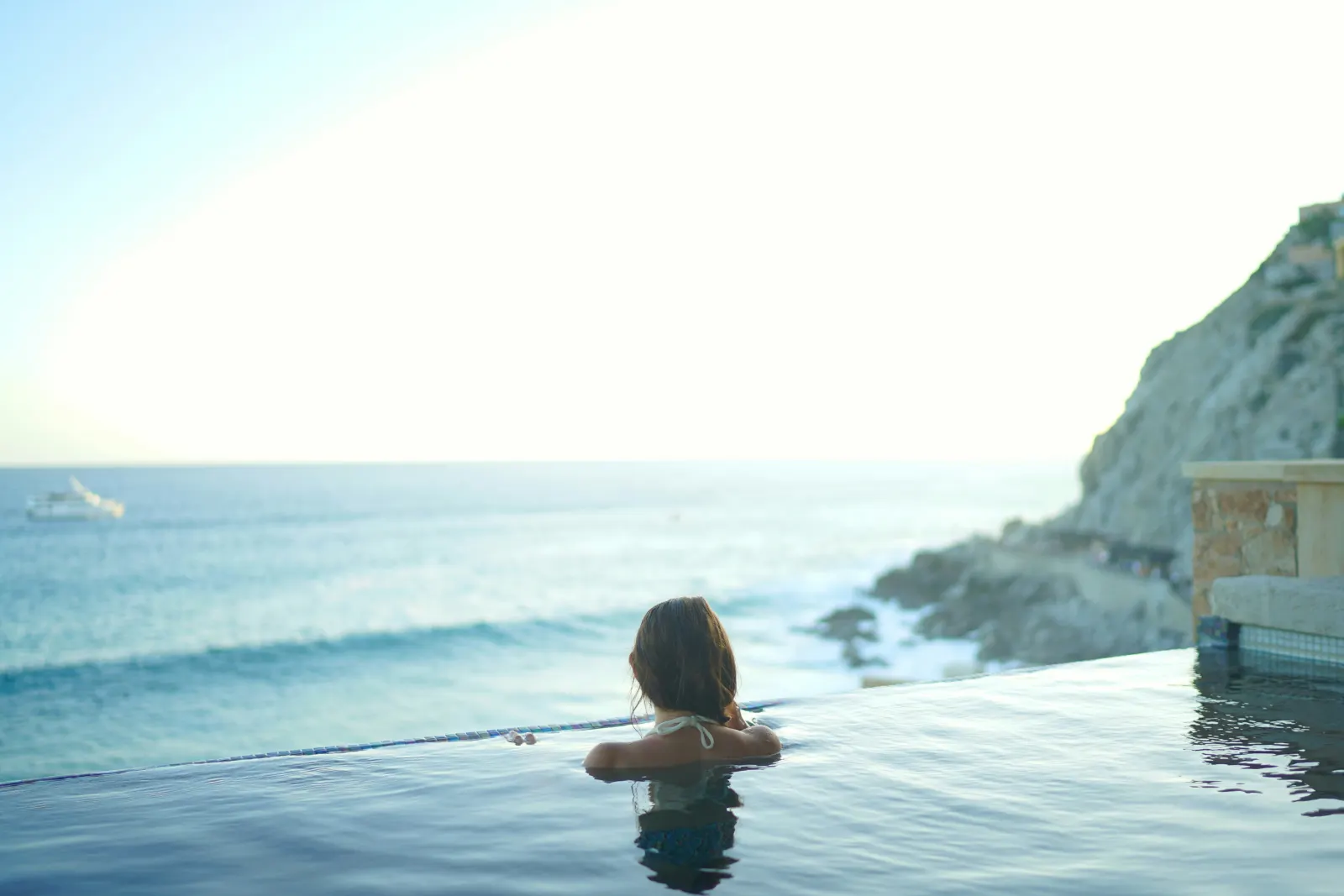 A swimmer at the edge of an infinity pool looking out over the sea in late afternoon light.