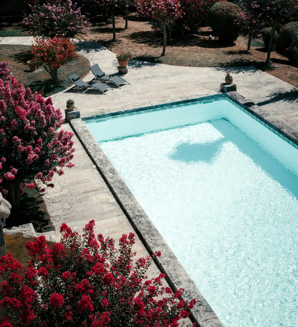 A pale limestone terrace beside a swimming pool in hard midday sun, the stone in full light and the water still.